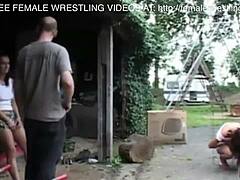 Two girls engage in a wrestling match in a car junkyard